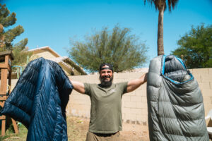 Josh Kirchner from Dialed in Hunter holding up a quilt and sleeping bag for backpack hunting