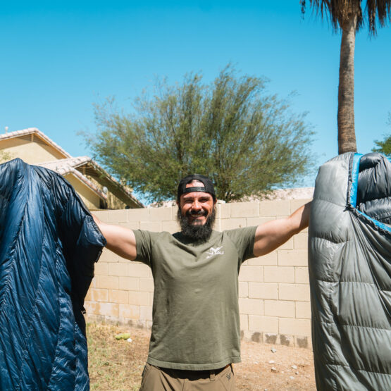 Josh Kirchner from Dialed in Hunter holding up a quilt and sleeping bag for backpack hunting